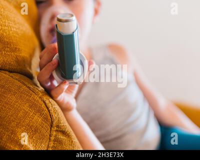 Vista laterale del contenuto ragazzo malato utilizzando respiratore e respirare ossigeno da inalatore mentre si siede sul divano a casa Foto Stock