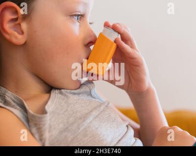 Vista laterale del contenuto ragazzo malato utilizzando respiratore e respirare ossigeno da inalatore mentre si siede sul divano a casa Foto Stock