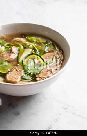 Ciotola di tradizionale zuppa vietnamita Pho bo noodle con foglie di basilico e lime posta su tavolo di marmo in sala luminosa Foto Stock