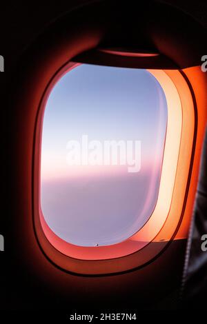 Attraverso la finestra dell'aeroplano che vola sopra le nuvole fluffy nel cielo blu del tramonto Foto Stock