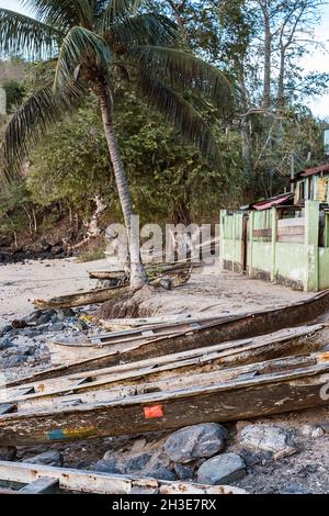 Fila di barche di legno invecchiate ormeggiate sulla spiaggia di sabbia dell'oceano contro piante tropicali verdi su São Tomé e Príncipe isola in giorno di sole Foto Stock