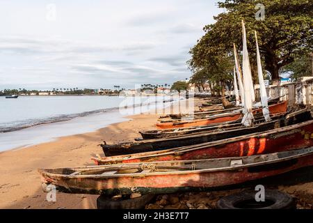 Fila di barche di legno invecchiate ormeggiate sulla spiaggia di sabbia dell'oceano contro piante tropicali verdi su São Tomé e Príncipe isola in giorno di sole Foto Stock