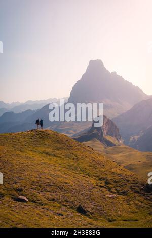 Escursionisti remoti anonimi in piedi su una collina erbosa mentre si ammira la ruvida catena montuosa contro il cielo nuvoloso nella natura della Spagna Foto Stock