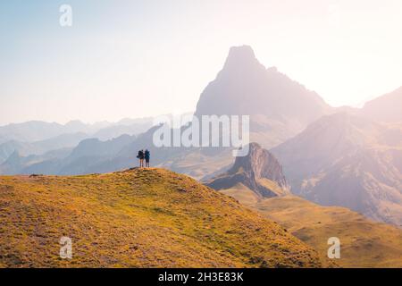 Escursionisti remoti anonimi in piedi su una collina erbosa mentre si ammira la ruvida catena montuosa contro il cielo nuvoloso nella natura della Spagna Foto Stock