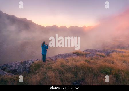 Vista posteriore di lontano irriconoscibile turista in piedi su terreno erboso circondato da montagne ruvide nella natura della Spagna in tempo nebbroso Foto Stock