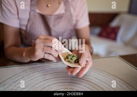 Dall'alto di raccolto irriconoscibile Donna in abiti casual e grembiule ripieno gnocchi con carne mentre preparando tradizionale cinese jiaozi in cucina Foto Stock