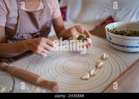 Dall'alto di raccolto irriconoscibile Donna in abiti casual e grembiule ripieno gnocchi con carne mentre preparando tradizionale cinese jiaozi in cucina Foto Stock