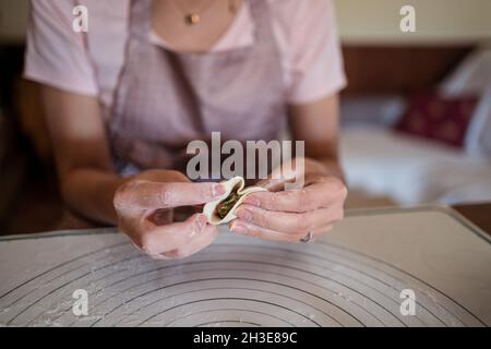 Dall'alto di raccolto irriconoscibile Donna in abiti casual e grembiule ripieno gnocchi con carne mentre preparando tradizionale cinese jiaozi in cucina Foto Stock