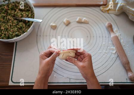Da sopra di raccolto anonimo cuoco femminile farcire l'impasto con carne mentre si preparano gnocchi cinesi tradizionali in cucina Foto Stock