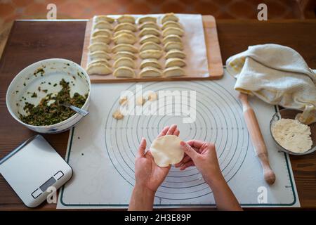 Da sopra di raccolto anonimo cuoco femminile farcire l'impasto con carne mentre si preparano gnocchi cinesi tradizionali in cucina Foto Stock