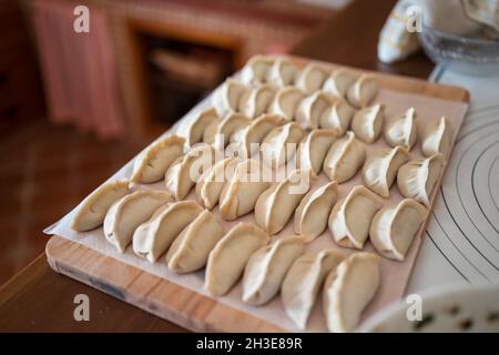 Da sopra di gnocchi tradizionali jiaozi crudi serviti su tagliere di legno in cucina Foto Stock