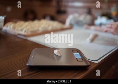 Dall'alto del pezzo di pasta messo su scala elettronica vicino al raccolto anonimo Donna che prepara gnocchi jiaozi Foto Stock