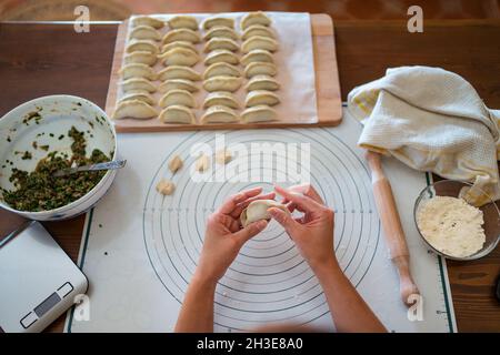 Dall'alto di raccolto irriconoscibile Donna in abiti casual e grembiule ripieno gnocchi con carne mentre preparando tradizionale cinese jiaozi in cucina Foto Stock