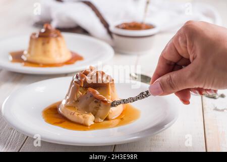 Crop irriconoscibile femmina mangiare dolce crema di uova con dulce de leche su piatto bianco servito su tavola di legno in cucina Foto Stock