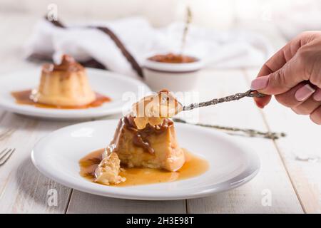 Crop irriconoscibile femmina mangiare dolce crema di uova con dulce de leche su piatto bianco servito su tavola di legno in cucina Foto Stock