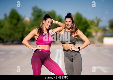 Gemelle in forma positiva in abbigliamento sportivo in piedi insieme su asfalto e guardando la macchina fotografica in giornata di sole Foto Stock
