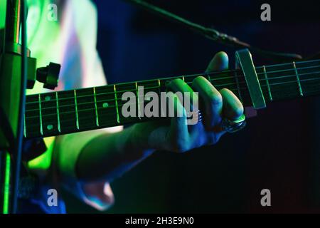 Chitarrista femminile ritagliato e irriconoscibile che suona la chitarra acustica in un club di luci Foto Stock