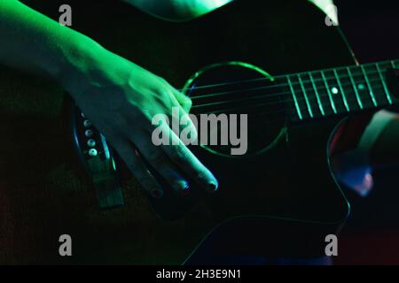 Chitarrista femminile ritagliato e irriconoscibile che suona la chitarra acustica in un club di luci Foto Stock