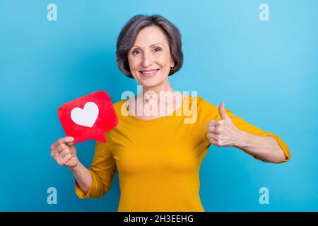 Ritratto di anziano pensionato pensionato ragazza allegra tenuta in mani come carta mostrando thumbup isolato su sfondo di colore blu brillante Foto Stock