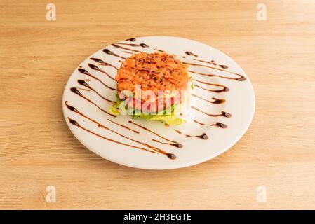 Tartare di salmone norvegese, strato di cubetti di pomodoro e lattuga cpa con salsa di soia su piatto bianco Foto Stock