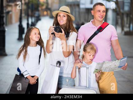 Sorridente famiglia di turisti che camminano in città e usando la mappa Foto Stock