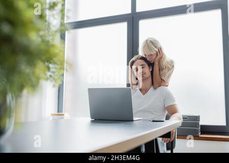 donna bionda stroking capelli di ragazzo felice che lavora da casa Foto Stock