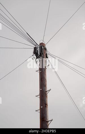 Vista ad angolo basso di un palo telegrafo in legno con fili che portano alle case locali fornendo segnali di telecomunicazione per telefoni domestici e a banda larga Foto Stock