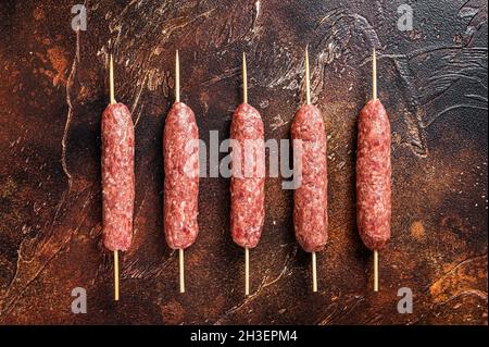 Kebab crudo di carne kofta salsicce su spiedini. Sfondo scuro. Vista dall'alto Foto Stock