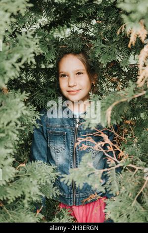 ritratto del volto di una bella caucasica caucasica candida sana bambina di otto anni circondato da rami e foglie di verde thuja pianta o cypres Foto Stock