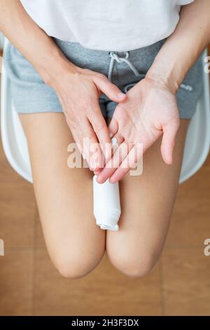 La ragazza tiene un vaso di crema di lividi nelle sue mani. La ragazza spalma la crema sulle mani. Vista dall'alto Foto Stock