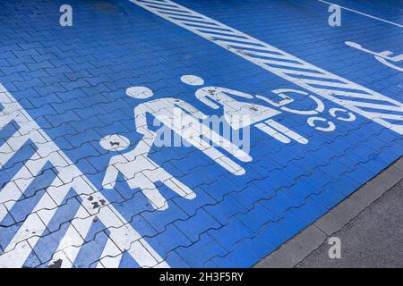 Il pittogramma che mostra i genitori con i bambini è stato dipinto di bianco su una superficie blu. Il cartello indica un posto auto riservato ai genitori con bambini. Foto Stock