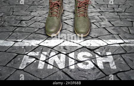Vista dall'alto - scarpe su ciottoli davanti alla linea con il testo Finish. Il concetto di finitura, finitura, riassumendo. Foto Stock
