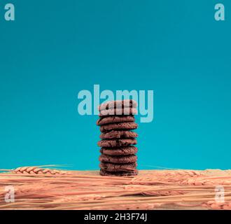 Biscotti all'uvetta al cioccolato impilati con steli di orzo secco su sfondo blu vintage. Stile retrò vintage, vita morta, arte da parete Foto Stock