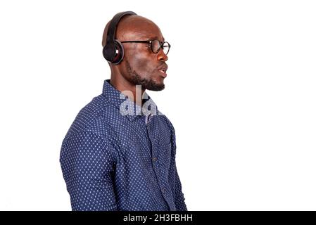 Uomo adulto serio e bello che indossa gli occhiali e ascolta la musica con le cuffie che guardano lateralmente Foto Stock