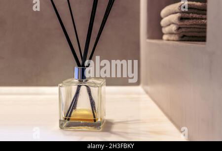 Diffusore reed in bagno, bastoncini neri in bottiglia di vetro, fragranza per la casa, deodorante per l'aria. Asciugamani ripiegati sulla mensola a muro, spa interio dal design moderno Foto Stock