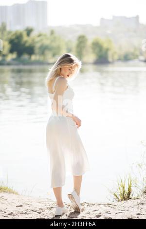 Una giovane donna si erge vicino al fiume. Bel modello in abito bianco svolazzante Foto Stock