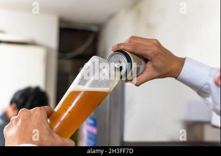 versa a mano la birra da una lattina in un bicchiere Foto Stock