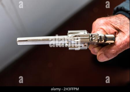 Una vecchia mano che tiene un revolver antico in una posizione di scatto Foto Stock