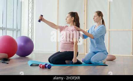 Assistente medico che aiuta la donna incinta a fare le esercitazioni della sfera Foto Stock