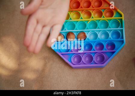 Il bambino gioca con il giocattolo e la nocciola pop. Gioco per lo sviluppo di abilità motorie. L'arcobaleno tocca il fidget sensoriale. Vista dall'alto. Foto di alta qualità Foto Stock