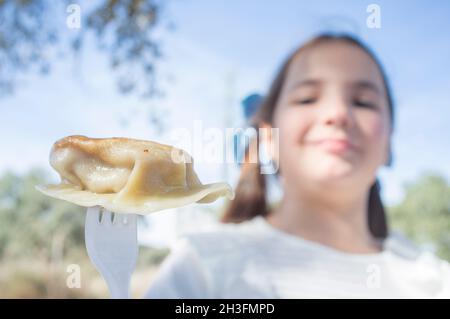 Bambina con jiaozi pezzo su forchetta. Sfondo esterno Foto Stock