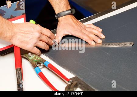 Un lavoratore segna un foglio di ferro da tetto con una matita e un righello di metallo. Primo piano delle mani di un lavoratore. Foto Stock