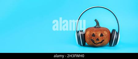 Zucca arancione con cuffie wireless bianche su sfondo blu. Halloween concetto e audio. Banner Foto Stock