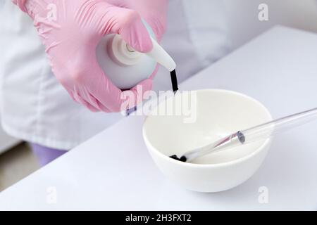 Primo piano del cosmetologo che riempie un contenitore con maschera nera per il peeling al carbonio Foto Stock