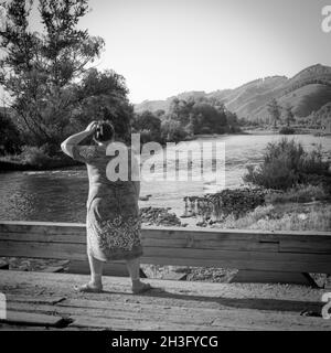 31 luglio, Russia, Altay, scena rurale con donna sul ponte che guarda su horison sullo sfondo delle montagne Foto Stock
