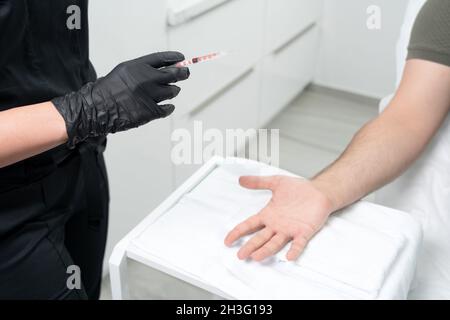 il medico fa un colpo di tossina botulinica nelle mani di un palmo maschio contro sudorazione eccessiva, trattamento di iperidrosi Foto Stock