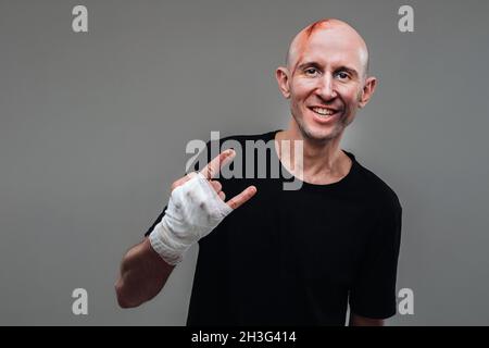 Su uno sfondo grigio si erge un uomo martellato in una T-shirt nera con le mani avvolte. Foto Stock