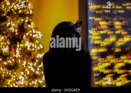 Silhouette di una ragazza con una corona di fronte all'albero di natale Foto Stock