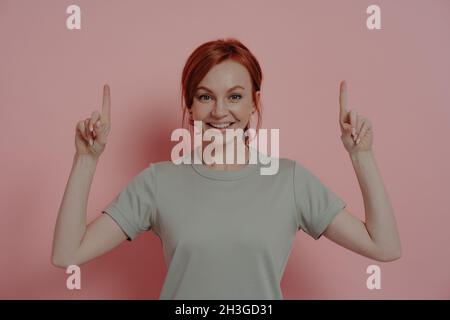 Felice giovane donna caucasica che punta verso l'alto con le dita indice e sorridente allegro Foto Stock