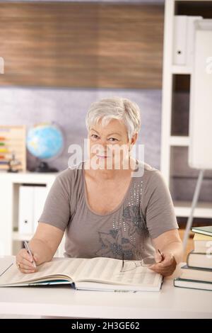 Insegnante senior a scuola alla ricerca di un libro Foto Stock